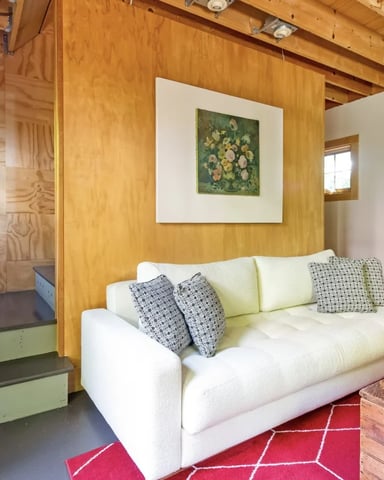 Loft bedroom with white sofa, wooden beams, exposed wood walls, and framed artwork on lavender walls