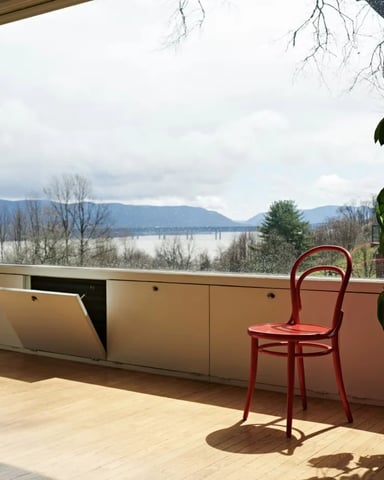 Modern room with large window overlooking lake and mountains, red chair, potted plant, wooden floor
