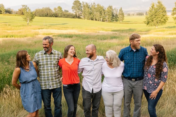 Seven people standing together in a grassy field with trees and rolling hills in the background